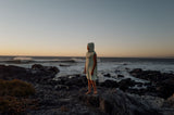 ION Grom 2025 Neoprenanzug, Frau trägt hellen Wetsuit am Strand bei Sonnenuntergang, Frontalansicht