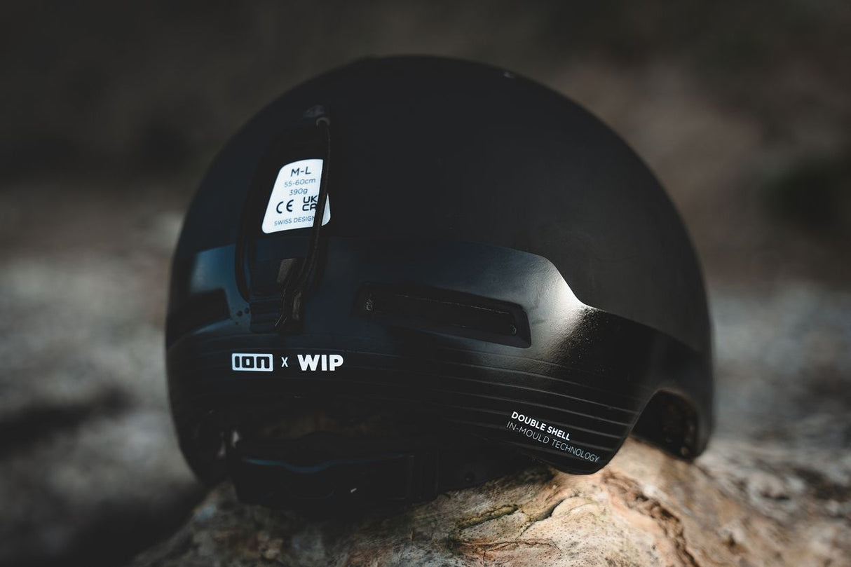 ION Mission 2026 Helm in Schwarz mit Visier, Seitenansicht auf Stein, modernes Kiteboarding-Design