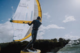 ION Mission 2026 Kite mit weißem Segel und gelben Streben, Kitesurfer in schwarzem Neoprenanzug auf dem Wasser in Aktion