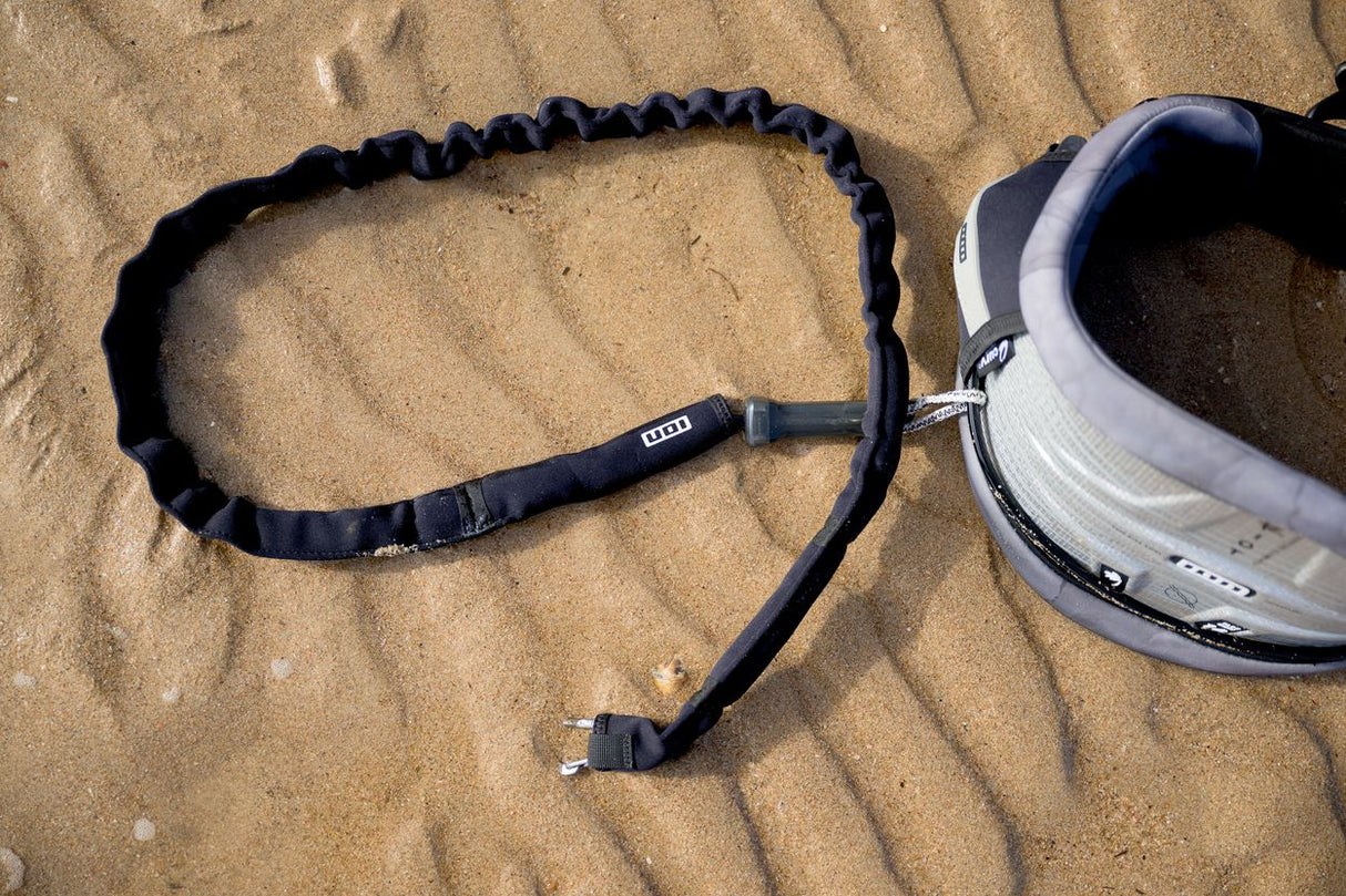 ION Handle Pass Leash Comp 2026 Trapezleash schwarz mit Elastik und Metallkarabiner am Sand