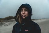 ION Neo Cosy Coat 2026 dunkelblau mit Kapuze, Frau trägt Neoprenjacke am Strand