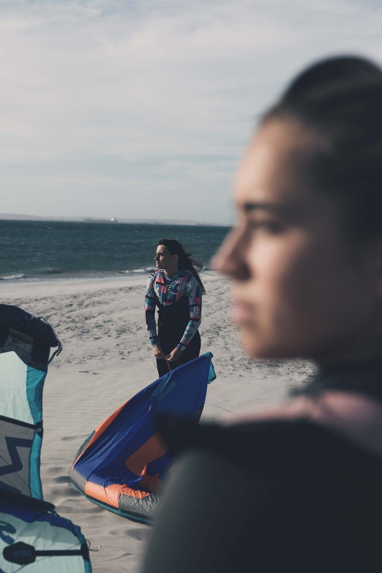 ION Ivy Weste Front Zip 2026 in Dunkelblau, Frontalansicht am Strand mit Kitesurfausrüstung