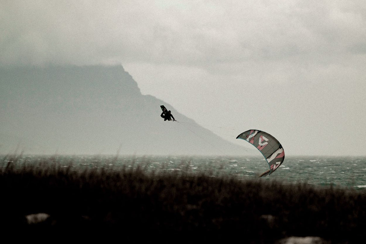 ION Amp Long 2026 Kite in Aktion über Wasser, Kitesurfer in Bewegung, grauer Himmel, Berglandschaft