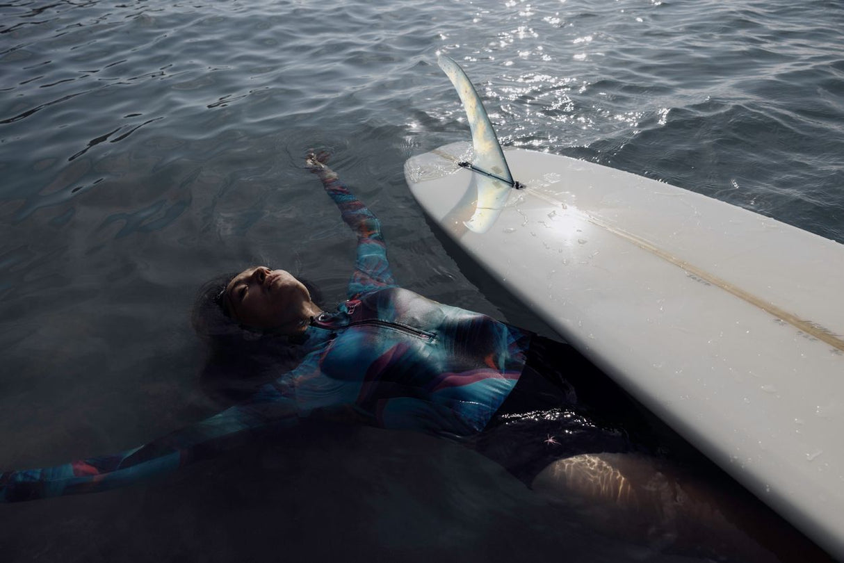 ION Badehose LS Damen 2024 blau, Langarm-Schwimmhose im Wasser neben Surfboard getragen
