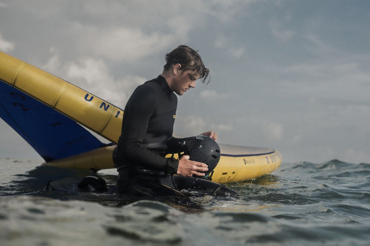 ION Slash Amp 2026 Kiteboard, schwarz-gelb, im Wasser bei Nutzung durch Wassersportler in Seitenansicht