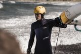 ION Slash Amp 2026 Kiteboard Neoprenanzug schwarz, Sportler trägt gelmen Helm am Strand mit Board