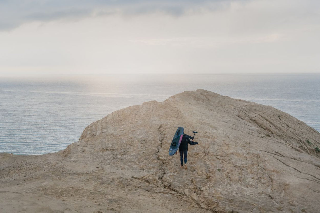 ION Neo Hoody Reversible 2026 Neoprenanzug in Blau, getragen beim Surfen am Strand mit Surfbrett