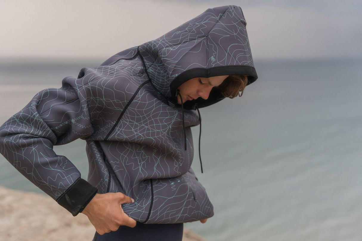 ION Neo Hoody Reversible 2026, Neopren-Jacke mit Kapuze, Grau mit Muster, wasserabweisend, Frontalansicht am Strand getragen