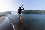 ION Neo Top 2/2 LS men schwarz, Kitesurfer trägt Neoprenanzug am Strand mit Kite und Board