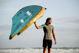ION Neo Top 2024 Kiteboard in Türkis und Gelb, von Person am Strand getragen, Frontalansicht