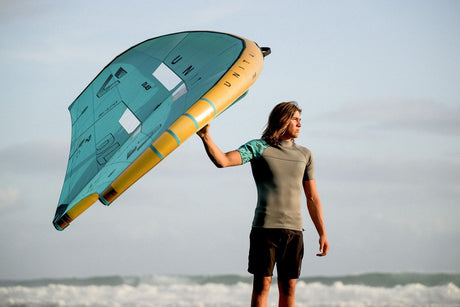 ION Neo Top 2024 Kiteboard in Türkis und Gelb, von Person am Strand getragen, Frontalansicht