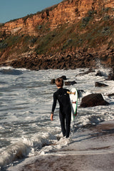 ION Capture Amp 4/3 Front Zip Junior Neoprenanzug schwarz, Kind trägt Wetsuit mit Surfboard am Strand
