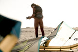 ION Apex Kite Trapez Herren 2026 in Braun, Athlet trägt Trapez am Strand mit Kite