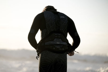 ION Apex Kite Trapez Herren 2026 in Schwarz, Frontalansicht mit Träger am Strand