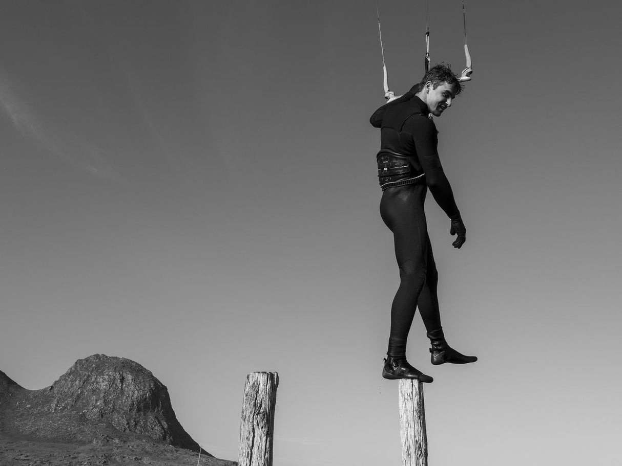 ION Spectre 2026 Kiteboard, schwarzes Sportgerät in Aktion, Kitesurfer springt mit Kite in Luftaufnahme vor Berglandschaft