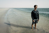 ION Surf Shield 2026 schwarzer Rashguard Langarm am Strand, Mann im Wasser tragend