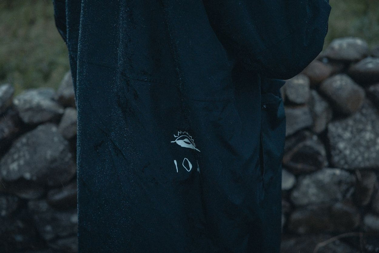 ION Storm Coat unisex 2026 in Dunkelblau mit Logo-Detail, Nahaufnahme des Materials und Branding auf Steinuntergrund