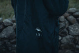 ION Storm Coat unisex 2026 in Dunkelblau mit Logo-Detail, Nahaufnahme des Materials und Branding auf Steinuntergrund