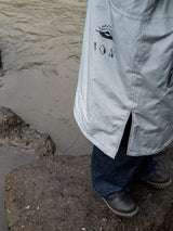 ION Storm Coat unisex 2026 in Hellgrau, Detailansicht mit ION-Logo, getragen am Strand