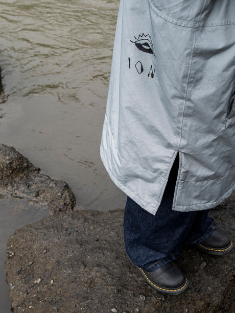 ION Storm Coat unisex 2026 in Hellgrau, Detailansicht mit ION-Logo, getragen am Strand