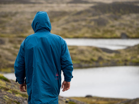 ION Storm Coat unisex 2026 in Blau, von hinten, mit Kapuze, in bergiger Landschaft
