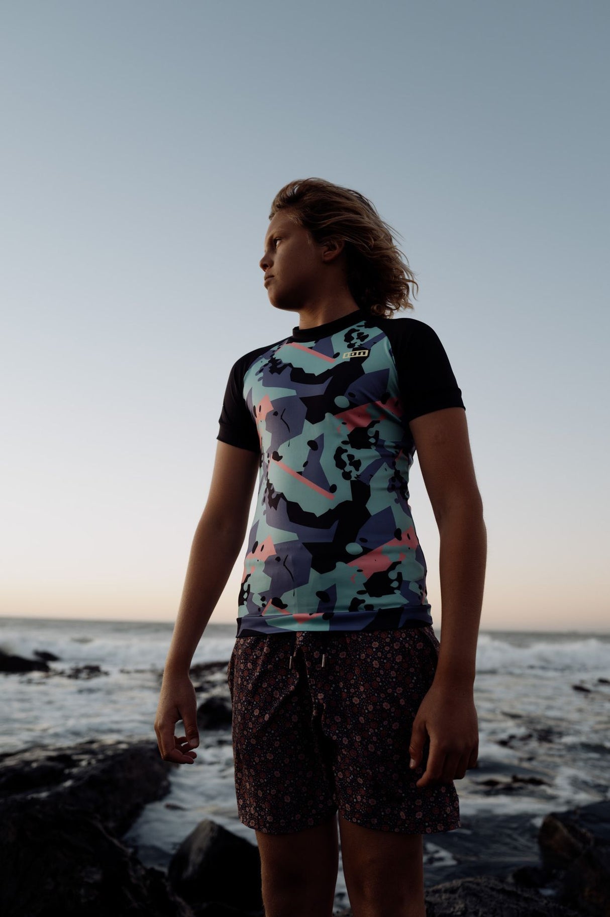 ION Rashguard Capture 2026, schwarzes Shirt mit buntem Muster, Frontansicht am Strand getragen