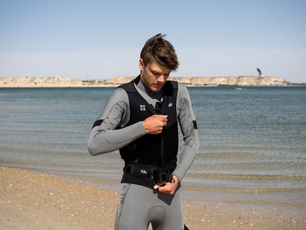 ION Rush Wing Vest 2026 schwarz, Frontansicht, Mann am Strand beim Anziehen der Weste