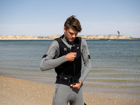 ION Rush Wing Vest 2026 schwarz, Frontansicht, Mann am Strand beim Anziehen der Weste