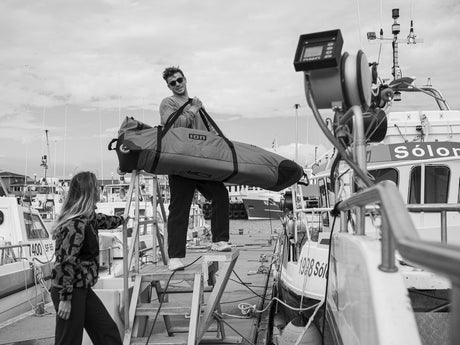 ION Kite Gearbag Core 2026 schwarz, Mann trägt aufgerollte Tasche auf Bootsanleger, Wassersportzubehör