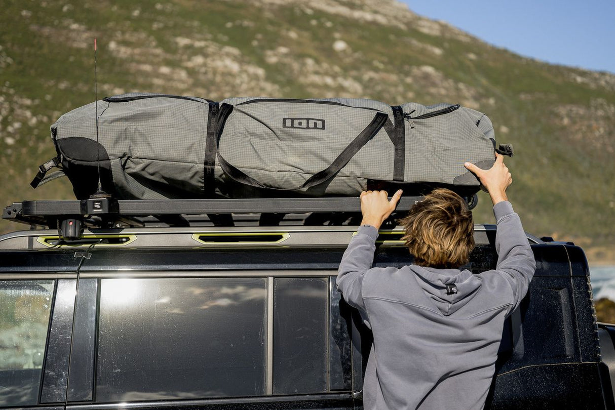 ION Wing Gearbag Core 2024 grau auf Autodachträger, Person befestigt Tasche mit Riemen