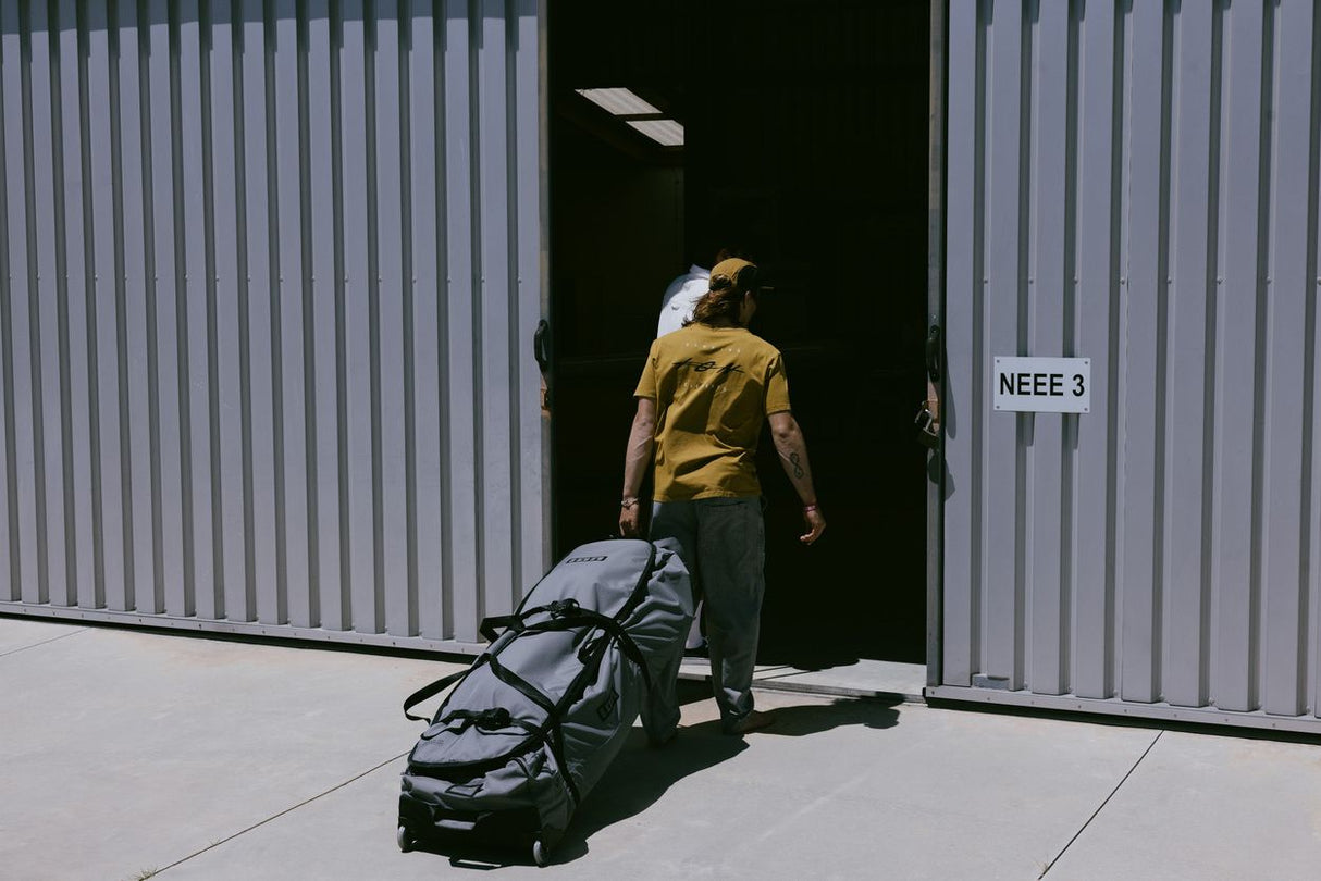 ION Surf Boardbag Core 2024 Tasche in Schwarz, mit Rollen, Transportansicht vor Lagerhalle