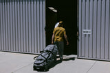 ION Surf Boardbag Core 2024 Tasche in Schwarz, mit Rollen, Transportansicht vor Lagerhalle