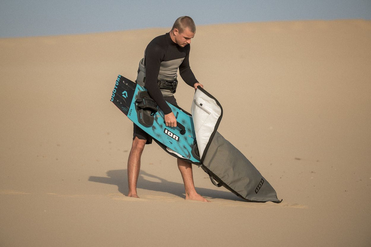 ION Twintip Boardbag Core 2024 grau, Mann mit Kiteboard und Boardbag am Strand, Schutzcase