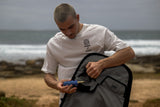 ION Twintip Boardbag Core 2024 schwarz, Mann öffnet Tasche am Strand, Frontalansicht