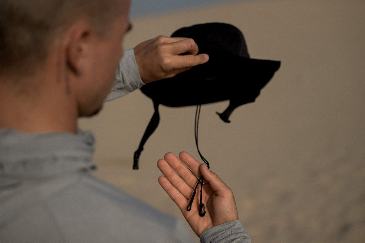 ION Beach Hat 2026 schwarzer Strandhut mit Kinnband, Person hält Hut in der Hand am Strand
