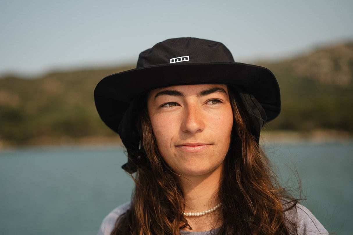 ION Beach Hat 2026 in Schwarz, Bucket-Hat-Stil mit breiter Krempe, getragen von Person am Wasser, Frontansicht