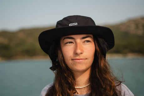 ION Beach Hat 2026 in Schwarz, Bucket-Hat-Stil mit breiter Krempe, getragen von Person am Wasser, Frontansicht