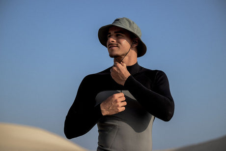 ION Bucket Surf Hat 2024 in Grau, getragen von Mann mit Kinnriemen, Frontalansicht vor blauem Himmel