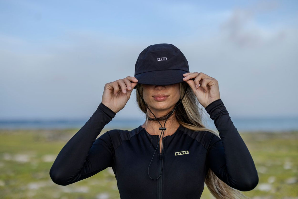 ION Bucket Surf Hat 2024 schwarz, Frontalansicht, Frau trägt schwarzen Bucket Hat am Strand mit Meereshintergrund