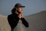 ION Surf Cap Pro 2026 schwarze Kappe mit Nackenschutz, seitliche Ansicht am Strand getragen