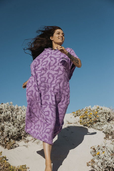 ION Surf Poncho Select Reefside 2024 in Violett mit geometrischem Muster, getragen am Strand