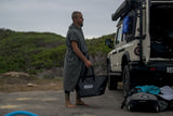 ION Surf Poncho Element 2026 grau, Wechselrobe aus Baumwollmischung, Mann trägt Poncho am Strand neben Campervan