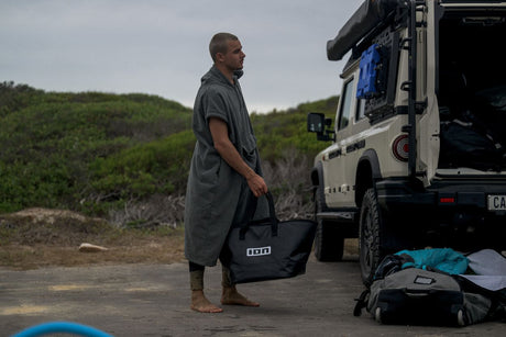 ION Surf Poncho Element 2026 grau, Wechselrobe aus Baumwollmischung, Mann trägt Poncho am Strand neben Campervan
