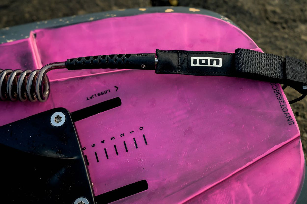 ION Wing Board Leash Core Coiled Knee 2026 schwarze Kabelschlaufe mit Spiralwicklung auf rosa Kiteboard, Draufsicht