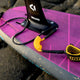 ION Wing Board Leash Core Hybrid Ankle 2026, schwarzes Neopren mit gelbem Kunststoffverschluss, auf magentaboard liegend
