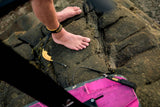 ION Wing Board Leash Core Hybrid Ankle 2026 schwarz-pink am Fuß getragen, Trageansicht mit Kite im Hintergrund