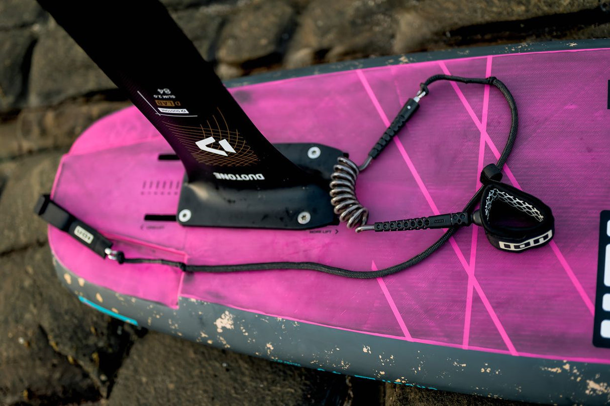 ION Wing Board Leash Core Hybrid Ankle 2026 schwarz auf pinkem Kiteboard, Hybrid-Design mit Spiralwindung, Detailansicht