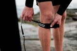 ION Wing Board Leash Core Hybrid Knee 2026, schwarzes Knieleash mit Hybrid-Material, an Bein angelegt, am Strand getragen