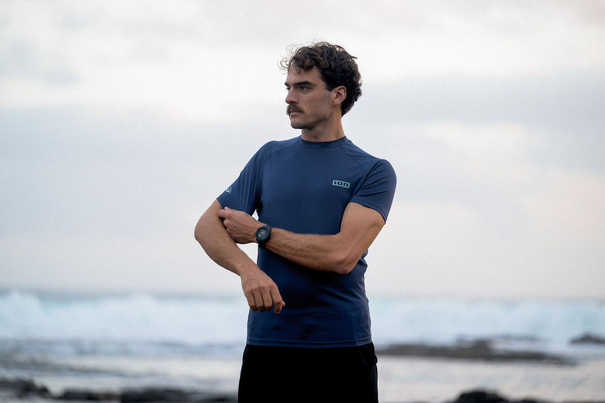 ION Rashguard SS 2024 dunkelblau, Kurzarm-Badeshirt aus Funktionsmaterial, Frontansicht an einem Mann am Strand getragen