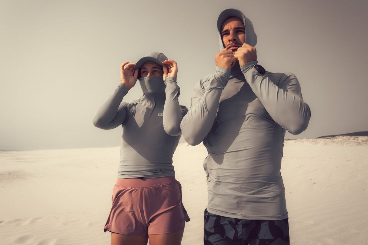 ION Rashguard Sun Pro SS26 mit Kapuze in Grau, langärmelig, am Strand getragen, Frontalansicht von zwei Personen